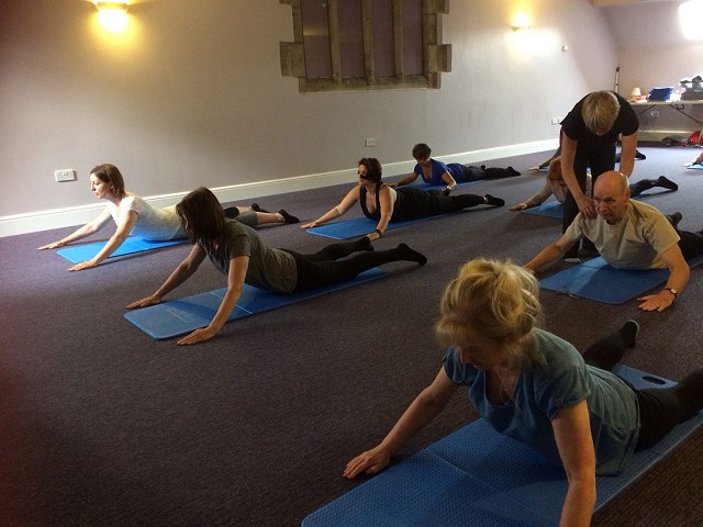 a group of pilates students performing the cobra; lying on their front with arms outstreached, rearing up on their forearms.